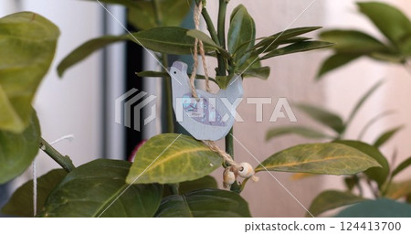 Brightly colored decorative Easter bird hangs from a lively green tree branch in a cozy indoor setting during daylight hours, creating a warm and cheerful atmosphere perfect for nature lovers 124413700