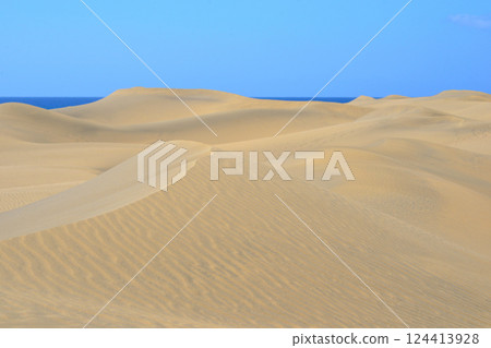 Sand dune with a sea at the background in Maspalomas, Gran Canaria. Sand barkhan with a wavy pattern Sand dune with a sea at the background in Maspalomas, Gran Canaria. Sand barkhan with a wavy pattern 124413928