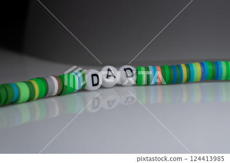 Close-Up Image of Colorful Beaded Bracelet Spelling "Dad" on Glossy Surface Reflective Background 124413985