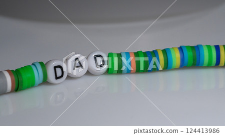 Colorful Handmade Bracelet with Letter Beads Spelling "Dad" on Gray Surface 124413986