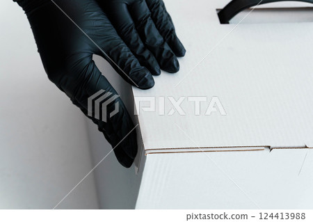 Close-up of Black Gloved Hands Carefully Handling White Cardboard Box Packaging Close-up of Black Gloved Hands Carefully Handling White Cardboard Box Packaging 124413988