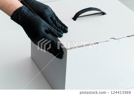 Gloved Hands Securing White Cardboard Box for Safe Delivery and Handling 124413989