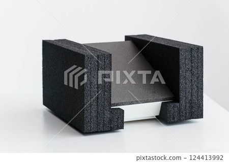 Angular Gray Object Resting Between Two Textured Black Foam Supports on White Surface 124413992