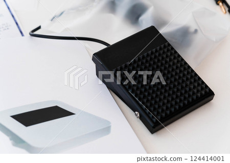 Close-Up View of Black Foot Pedal Switch on Desk with Electronic Device and Cables Close-Up View of Black Foot Pedal Switch on Desk with Electronic Device and Cables 124414001