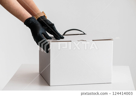 Hands in Black Gloves Carefully Closing White Cardboard Box on White Table Hands in Black Gloves Carefully Closing White Cardboard Box on White Table 124414003