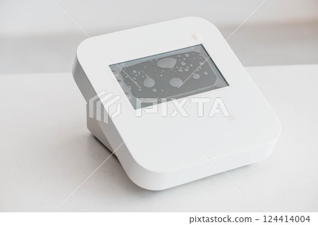 Modern White Digital Device with Display Showing Water Droplets on Screen Modern White Digital Device with Display Showing Water Droplets on Screen 124414004