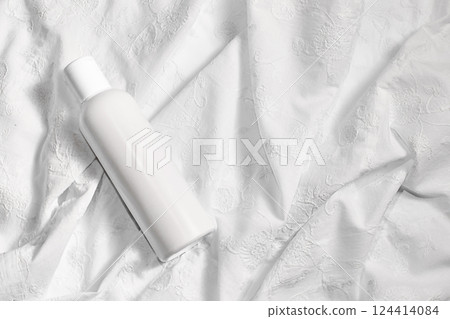 White cosmetic bottle on white fabric with space for text. White cosmetic bottle on white fabric with space for text. 124414084