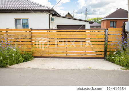 Wooden fence with closed gate and flowers in front of house. Closed access, natural border, and welcoming suburban entrance design 124414684
