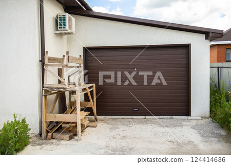 Woodwork and scaffolding in front of brown garage door. Exterior home renovation and tidy, building storage Woodwork and scaffolding in front of brown garage door. Exterior home renovation and tidy, building storage 124414686