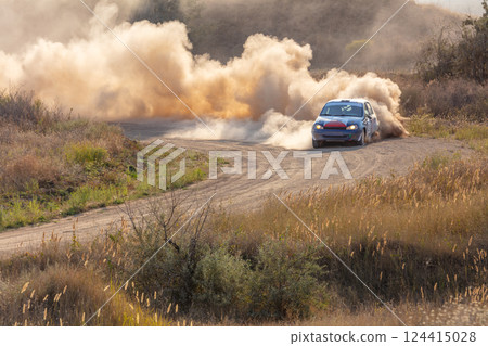 Rally Car on a Turn and a Cloud of Dust in the Sunlight 124415028