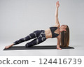 Calm female in activewear doing variation of side plank with bent leg indoors. Side view of barefoot sportswoman practicing side plank yoga position, isolated on grey background. Yoga concept. 124416739