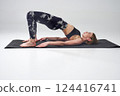 Mindful slim woman in leggings doing bridge position of yoga. Side view of barefoot female in activewear in Setu Bandhasana yoga pose on mat, during training, isolated on grey. Concept of yoga.  124416741