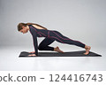 Flexible woman in black bodysuit exercising on yoga man in studio. Side view of concentrated brunette girl wearing tight sportswear, practicing yoga asana, isolated on grey. Concept of yoga. 124416743