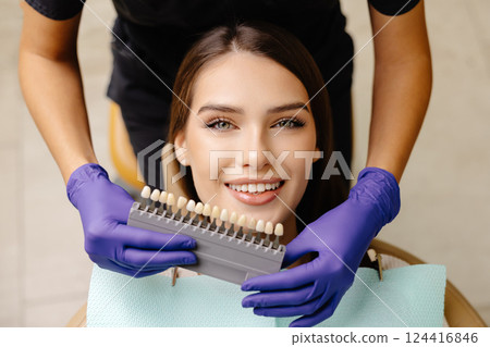 Dentist choosing teeth enamel shade color for young smiling female patient before whitening procedure 124416846