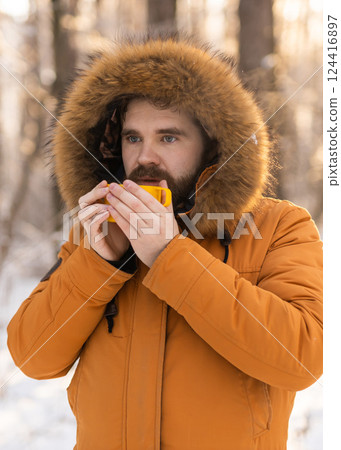 Man drinking from yellow cup in snowy forest. Reflects winter survival, daily rituals and connection between warmth and mindfulness outdoors. Copy space 124416897