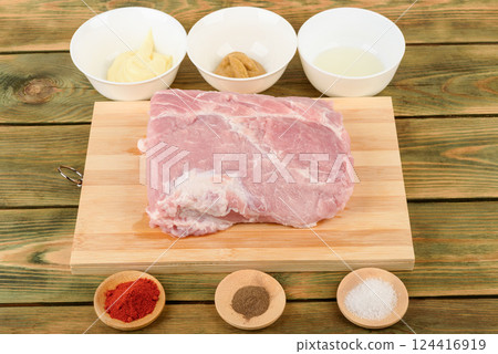 Raw pork meat on a cutting board and spices for marinade. 124416919
