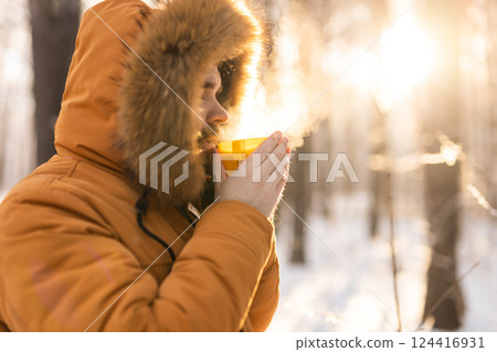 Man drinking from yellow cup in snowy forest. Reflects winter survival, daily rituals and connection between warmth and mindfulness outdoors. Copy space Man drinking from yellow cup in snowy forest. Reflects winter survival, daily rituals and connection between warmth and mindfulness outdoors. Copy space 124416931