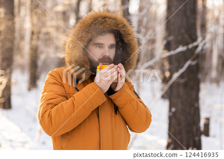 Man drinking from yellow cup in snowy forest. Reflects winter survival, daily rituals and connection between warmth and mindfulness outdoors. Copy space 124416935