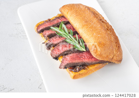 Grilled ciabatta sandwich with melted cheese, juicy steak, caramelized onions, and rosemary 124417028