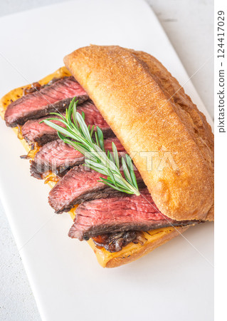 Grilled ciabatta sandwich with melted cheese, juicy steak, caramelized onions, and rosemary 124417029