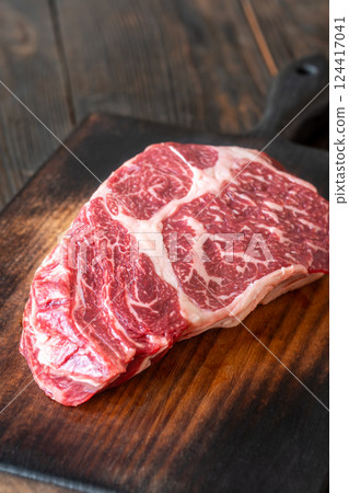 Raw ribeye steak on a wooden board with coarse salt and peppercorn Raw ribeye steak on a wooden board with coarse salt and peppercorn 124417041