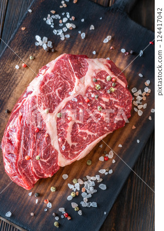 Raw ribeye steak on a wooden board with coarse salt and peppercorn 124417042