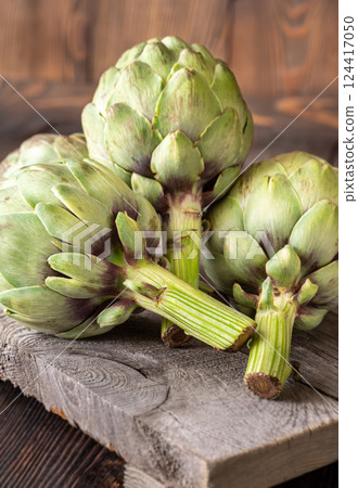 Fresh raw artichokes on vintage cutting board with rustic wooden background texture Fresh raw artichokes on vintage cutting board with rustic wooden background texture 124417050