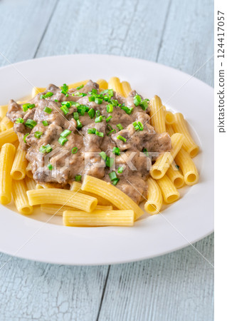 Beef stroganoff with rigatoni pasta, topped with fresh green onion garnish 124417057
