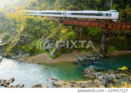 穿梭在朝陽照耀下的山谷中的福知山線特快列車 穿梭在朝陽照耀下的山谷中的福知山線特快列車 124417127