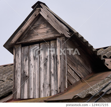 Weathered wooden dormer window on an old tiled roof. The aged wood and peeling paint Weathered wooden dormer window on an old tiled roof. The aged wood and peeling paint 124417235
