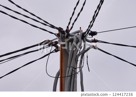 Electrical pole with numerous tangled cables and wires. The infrastructure appears chaotic, with various connectors and insulators visible 124417238