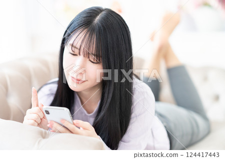 A young woman lying down and operating a smartphone at home A young woman lying down and operating a smartphone at home 124417443