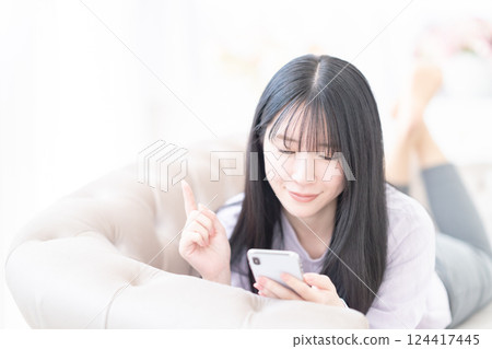 一位年輕女子在家中躺著操作智慧型手機 124417445