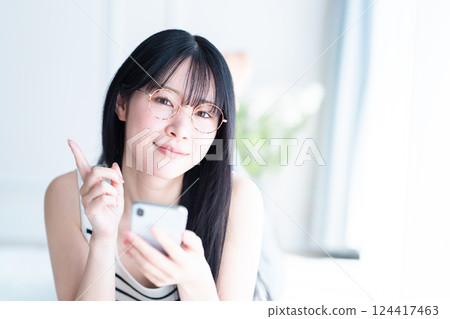 A young woman wearing glasses lying down and operating a smartphone 124417463
