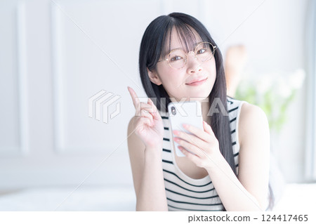 A young woman wearing glasses lying down and operating a smartphone 124417465