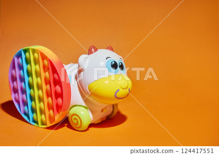 Baby kids toys orange background with copy space. Multi-colored rainbow pop can reduce stress and anxiety in children and adults. Plasmassovaya cute cow. 124417551
