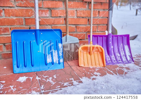 Colorful plastic snow shovels stand near the brick wall of the mansion Family concept of cleaning the house and the area around the house. 124417558