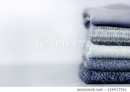 A stack of knitted jumpers and sweaters on a gray concrete blurry background. A stack of knitted jumpers and sweaters on a gray concrete blurry background. 124417561