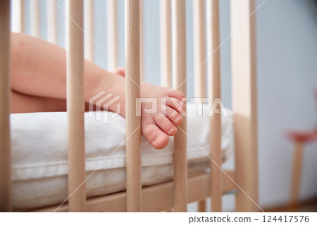 The baby's leg hangs from the child's wooden bed. The baby's leg hangs from the child's wooden bed. 124417576