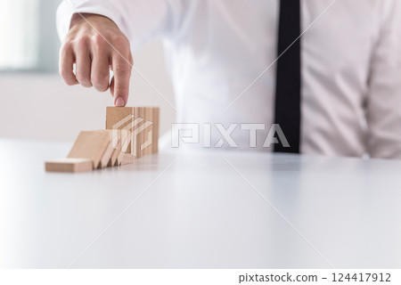 Business man interrupting domino effect by stopping wooden dominoes bricks Business man interrupting domino effect by stopping wooden dominoes bricks 124417912