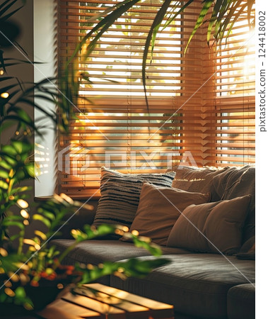 Warm sunlight streaming through wooden blinds, casting soft shadows on a sofa and a green palm leaf 124418002
