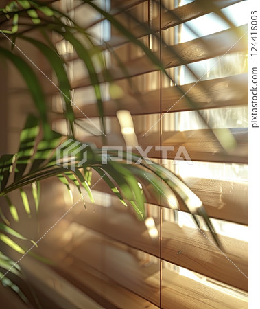 Warm sunlight streaming through wooden blinds, casting soft shadows on a sofa and a green palm leaf 124418003