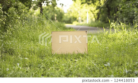a blank yard sign on a grassy area near a city street path, surrounded by trees and urban elements 124418053