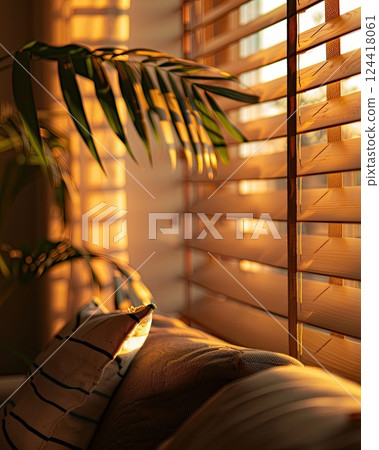 Warm sunlight streaming through wooden blinds, casting soft shadows on a sofa and a green palm leaf 124418061