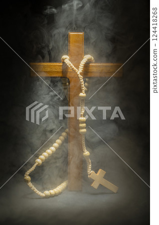 Wooden Christian cross and rosary beads on dark background. Light and smoke or fog effect. Symbol of religious and worship in God. Concept of Hope, faith, and religion Wooden Christian cross and rosary beads on dark background. Light and smoke or fog effect. Symbol of religious and worship in God. Concept of Hope, faith, and religion 124418268