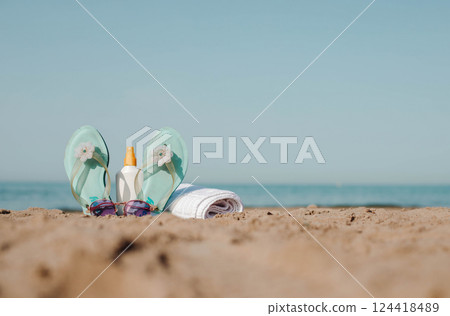 Beach sandals and sunscreen on sandy shore by the ocean Beach sandals and sunscreen on sandy shore by the ocean 124418489