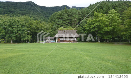 一棟傳統的茅草屋頂建築矗立在山脈和茂密的樹木之間的中心。 124418493
