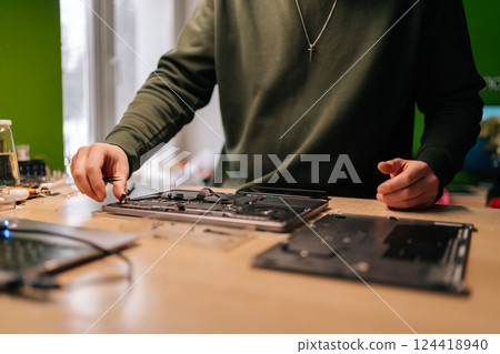 Cropped shot of electronic engineer using tweezers, fixing components on laptop motherboard, performing maintenance and troubleshooting in repair workshop. Concept of computer hardware, repairing. 124418940