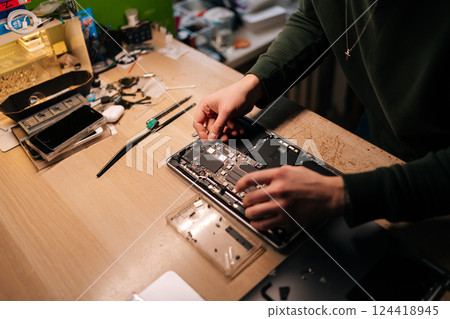 Top view of technician using tweezers repairing delicate laptop motherboard components in professional electronic workshop setting. Concept of computer hardware, repairing, upgrade, technology Top view of technician using tweezers repairing delicate laptop motherboard components in professional electronic workshop setting. Concept of computer hardware, repairing, upgrade, technology 124418945