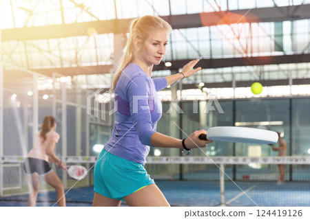 Sporty woman padel player hitting ball with a racket on hard court 124419126